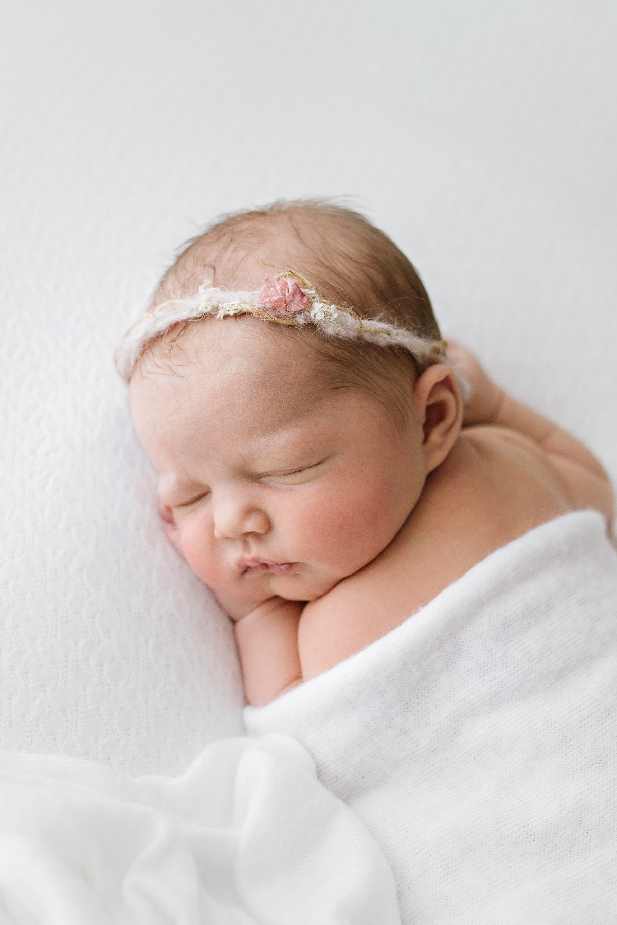 Newborn girl on a white blanket with a delicate flower headband - Kristy Notting Photography