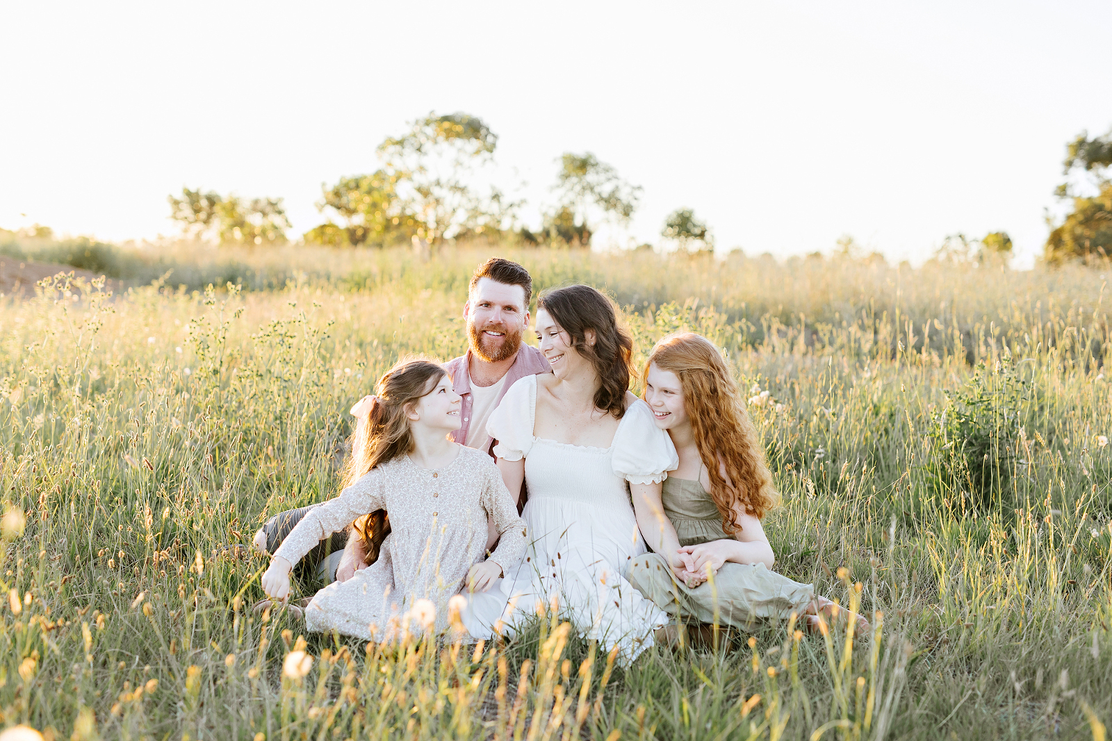 family sitting in a field laughing together- kristy notting photography