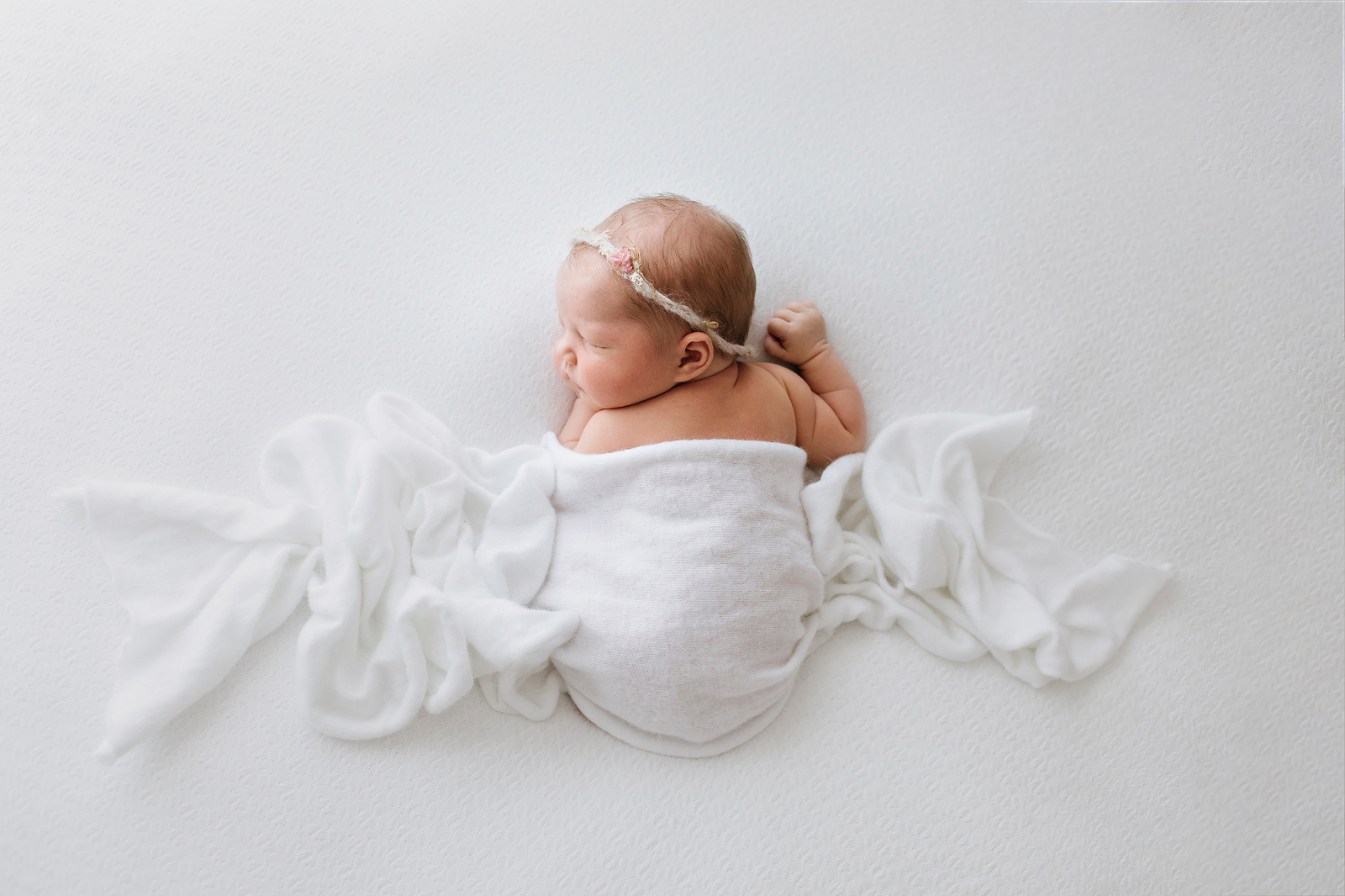 baby lying on a white blanket, covered with a white wrap-newborn-photographer-geelong