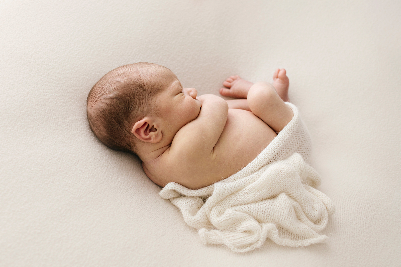 baby in a cream wrap, curled on a cream blanket-newborn-photographer-geelong