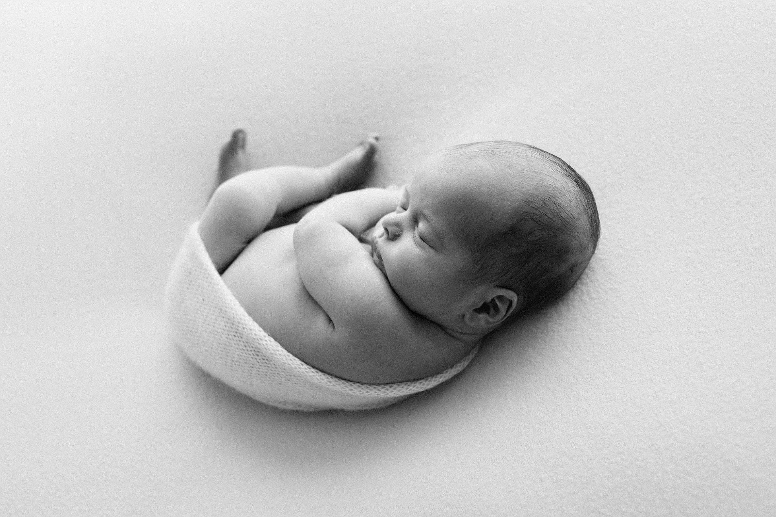 black and white image of a newborn baby curled up on a blanket