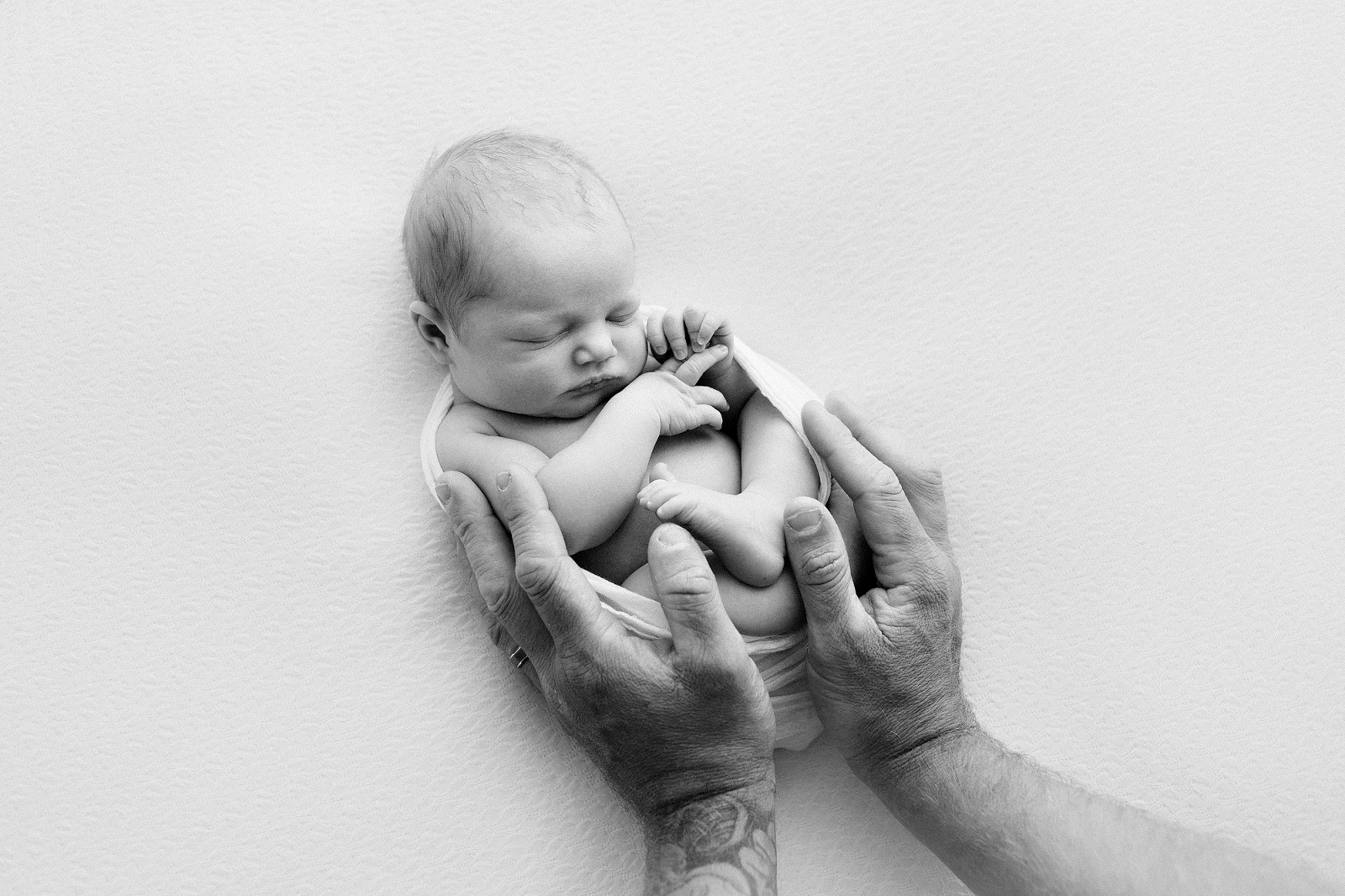 baby on a blanket with dad's hands
